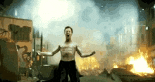 a man without a shirt is standing in front of a fire in a city .