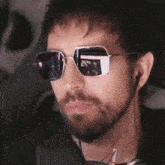 a man with a beard is wearing sunglasses and ear buds .