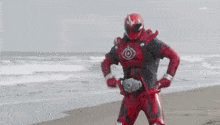 a man in a red superhero costume is holding a red sword on a beach .