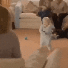 a baby is walking in a living room with a stuffed animal in his arms .