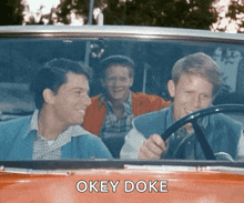three men are sitting in an orange car and one of them is holding a steering wheel and says " okey doke " .