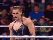 a woman is standing in a wrestling ring with a crowd behind her watching .