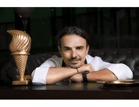 a man sits at a table with his arm resting on the table next to a gold ice cream cone