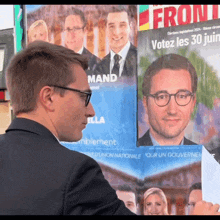 a man in a suit holds a piece of paper in front of a poster that says " votez les 30 juillet "