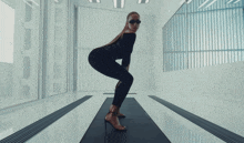 a woman in a black jumpsuit is standing on a mat in front of a large window