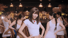 a woman in a white crop top stands in front of a group of girls