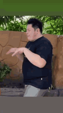 a man in a black shirt is standing in front of a wall .