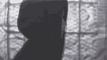 a person in a hooded jacket is standing in front of a window in a black and white photo .