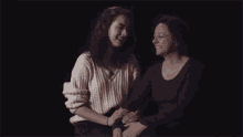two women are sitting next to each other in a dark room and holding hands .