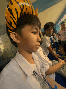 a boy wearing a tiger balloon on his head has a lanyard that says excelelea