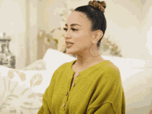 a woman wearing a green sweater and hoop earrings is sitting on a couch