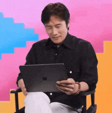 a man in a black shirt is sitting in a chair holding an apple tablet