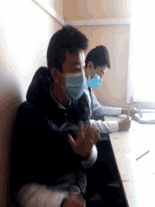 two young men wearing face masks sit at a table