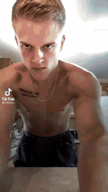a shirtless man with a tattoo on his chest looks at the camera with a tiktok icon above his head