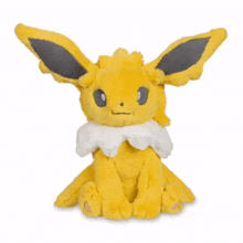 a yellow eevee stuffed animal with black ears is sitting on a white background .