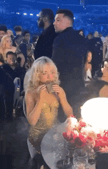 a woman in a gold dress is sitting at a table eating a sandwich .