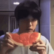 a man is eating a slice of watermelon in a kitchen .