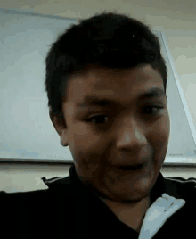 a young boy is making a funny face in front of a whiteboard