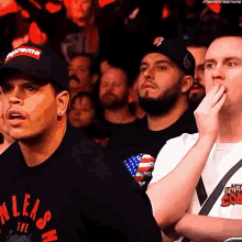 a group of men are sitting in a stadium watching a match . one of the men is wearing a supreme hat .