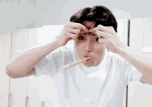 a young man in a white t-shirt is brushing his teeth