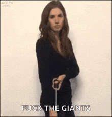 a woman in a black dress is holding a stick and saying `` fuck the giants '' .