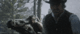 a man in a cowboy hat stands next to a horse in a forest .