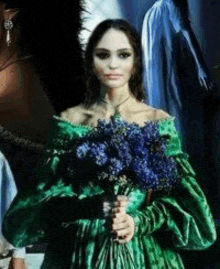 a woman in a green dress is holding a bouquet of purple flowers