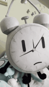a stuffed alarm clock with a sad face is laying on a bed next to other stuffed animals