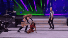 two women are wrestling in a wrestling ring with a referee standing behind them .