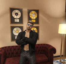 a shirtless man stands in front of a couch with a picture of a record on the wall behind him