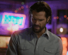 a man in a grey shirt stands in front of a neon sign that says ' lighting '