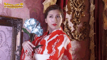 a woman in a red and white kimono is holding flowers in front of a wall with the word martial arts on it