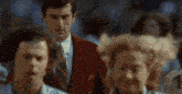 a man in a red suit and tie is walking through a crowd .