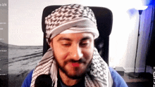 a man wearing a head scarf is sitting in front of a screen that says 2/6 on it