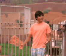 a man in a pink shirt is standing in front of a fence