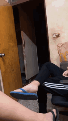 a person wearing flip flops sits on another person 's lap in a room