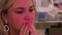 a close up of a woman with pink nails covering her mouth .