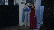 two women in long dresses standing next to each other in front of a door .