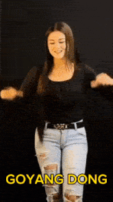 a woman in a black top and ripped jeans is dancing with the words goyang dong written in yellow