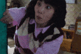a woman wearing a pink sweater and a striped vest is standing in a room