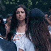 a woman in a white top with flowers on it stands in a crowd of people