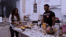 a man wearing a california shirt is standing next to a woman cutting food