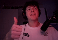 a man wearing headphones and a white nike shirt is giving a thumbs up