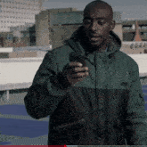 a man in a green and black jacket is looking at his cell phone
