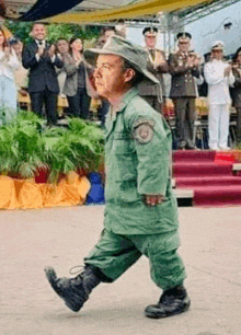 a man in a green military uniform is walking in front of a crowd of people