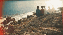 a group of people are sitting on rocks near the ocean looking at the water .