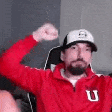 a man with a beard wearing a red jacket and a white hat is sitting in a chair .