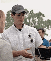 a man wearing a hat and sunglasses is talking to a woman on a film set .
