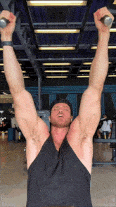 a man in a black tank top holds a barbell over his head