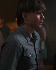 a young man in a striped shirt looks at the camera in a dark room